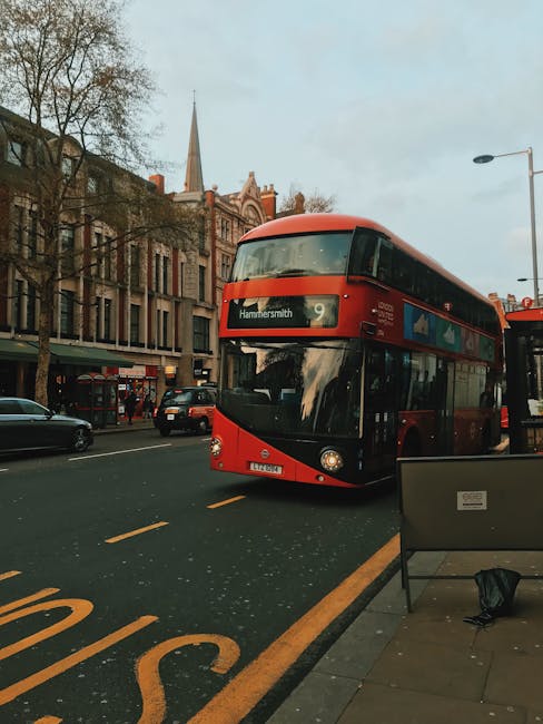A red double-decker bus displaying the route number 9 and the destination Hammersmith is traveling along a city street in Hammersmith, London, as part of local public transport services. The bus is ap